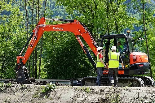 Mini-pelle sur un chantier et stagiaires en gilet, formation engins de chantier R482