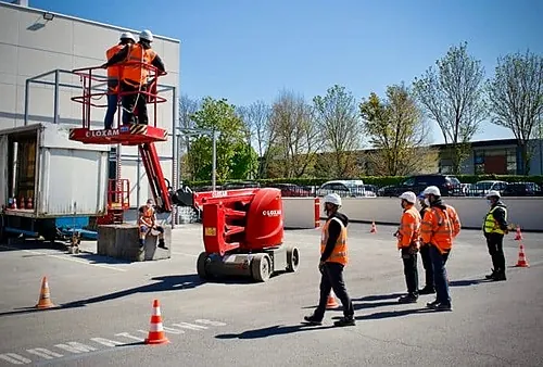 Nacelle élévatrice et stagiaires en gilet sur une aire balisée, formation PEMP R486